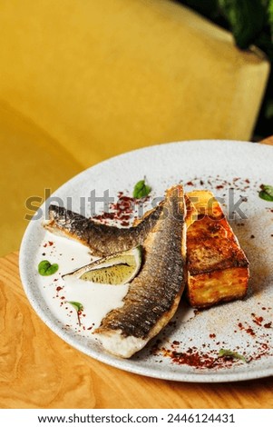 restaurant-style presentation of Seabass with potato gratin and celery sauce, elegantly served on a wooden table, yellow background. Perfect choice for culinary promotions and food enthusiasts
