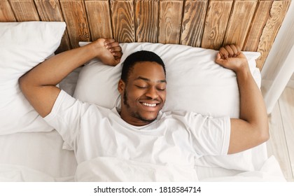 Rested African American Man Waking Up Stretching Hands Awakening Lying In Bed At Home In The Morning, Smiling With Eyes Closed. Good Sleep, Rest And Recreation Concept. Above View