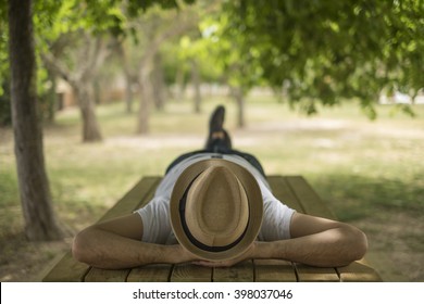 Restful young man wearing a straw hat laying down on a wooden table in the middle of the forest at a park - Powered by Shutterstock