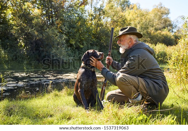 Resting after\
hunting. Good job, successful hunting on lake. Bearded man after\
hunting on ducks caress his\
dog