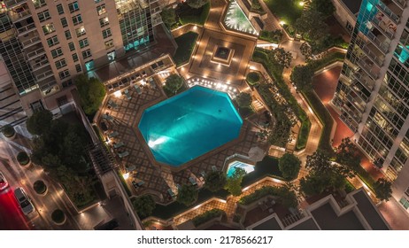 Resting Area Among Skyscrapers With Illuminated Swimming Pool And Sunbed In Dubai Downtown Night Timelapse. Aerial Top View From Above