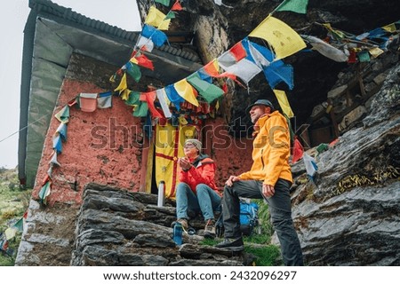 Resting Backpackers Couple tea break at small sacred Buddhist monastery decorated multicolored Tibetan prayer flags with mantras. Climbing Mera Peak route in Makalu Barun National Park, Nepal