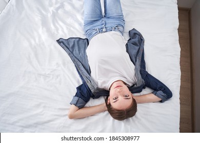 Resting in bed. Top view of the attractive young woman laying with her hands under her head and looking to the camera with peacful mood