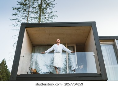 Resting Man Dressed White Bathrobe Standing On Forest House Balcony And Enjoying Fresh Air With Nature Forest Pine Trees View. Outside Scandinavian Interior Design House. Living In Wild Concept Image