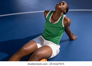 Resting on basketball court, female basketball player in green jersey relaxing. Sports, african american man, relaxation, leisure, training, fitness - Powered by Shutterstock