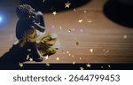 Resting seated Buddha figurine wearing golden robe on wood table at home, star overlays, copy space. Meditation, spirituality, tranquility, zen, decor, minimalist, harmony