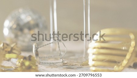 Resting silver muselet and two flute stems on tabletop, scattering gold foil, ribbon, star confetti. Champagne, macro, bokeh, stilllife, closeup, cork, wire