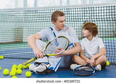 Resting Young Man Or Tennis Coach With Boy Sitting Near Net