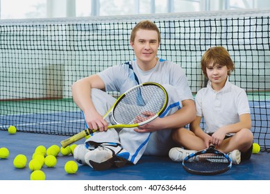 Resting Young Man Or Tennis Coach With Boy Sitting Near Net