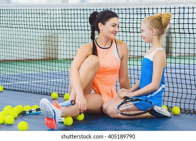 Resting Young Woman Or Tennis Coach With Girl Sitting Near Net