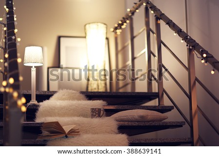 Resting-place with electric garland, cup of tea, book and lamps on modern stairs