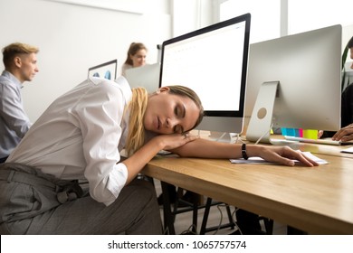 Restless young businesswoman sleeping at work desk, tired or bored female employee lying asleep at workplace at break, exhausted overworked office worker feeling lack of sleep or fatigue having nap