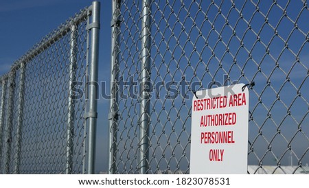 Restricted area, authorized personnel only sign in USA. Red letters, keep off warning on metal fence, United States border symbol. No trespassing notice means violators will be prosecuted by US law.