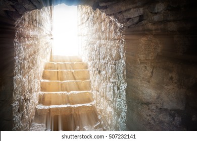Resurrection of Jesus Christ. Religious Easter background, with strong light rays shining through the entrance into the empty stone tomb. Artistic strong vignette, contrast, dramatic dark-light edit.