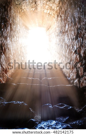 Resurrection of Jesus Christ. Religious Easter background, with strong light rays shining through the entrance into the empty stone tomb. Artistic strong vignette, contrast, dramatic dark-light edit.