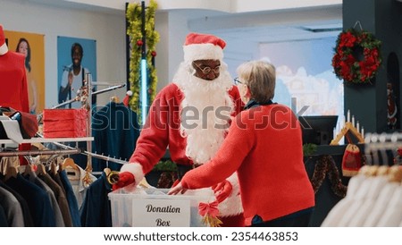 Retail assistant dressed as Santa Claus collecting unneeded clothes from clients in donation box, giving them as present to those in need during Christmas season, spreading holiday cheer