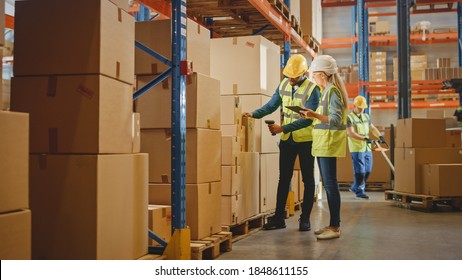 Retail Warehouse Full Of Shelves With Goods In Cardboard Boxes, Male Worker And Female Supervisor Holding Digital Tablet Discuss Product Delivery While Scanning Packages.Distribution Logistics Center