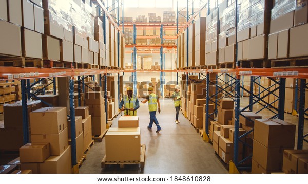 Retail Warehouse full of Shelves with Goods in
Cardboard Boxes, Workers Scan and Sort Packages, Move Inventory
with Pallet Trucks and Forklifts. Product Distribution Logistics
Center. Elevated Shot