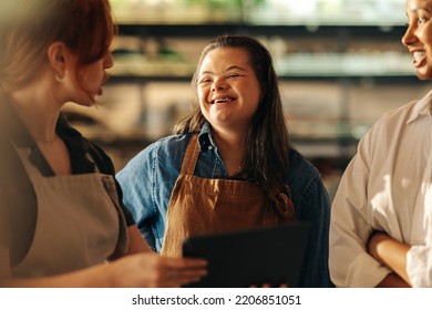 Retail Worker With Down Syndrome Smiling Happily While Standing In A Staff Meeting In A Grocery Store. Group Of Diverse Women Working Together In An All-female Small Business.