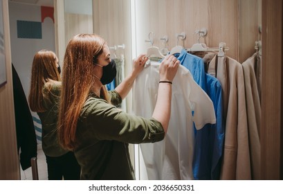 Retail Worker With Face Mask Working In Clothing Store, Sorting Clothes