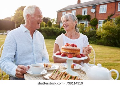 Retired Couple Enjoying Afternoon Tea In Garden At Home