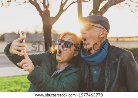retired couple enjoying free time taking funny selfie - middle-aged couple having fun together using smartphone - happy mature people take photos with mobile phone - sunny warm filter