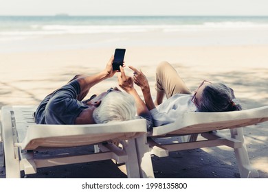 Retired Couple Resting On A Adirondack Chair By The Beach In The Sunlight And Clean Sandy Beach. Retirement Planning Ideas And Happy Life.