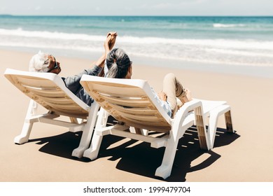 Retired Couple Resting On A Adirondack Chair By The Beach In The Sunlight And Clean Sandy Beach. Retirement Planning Ideas And Happy Life.