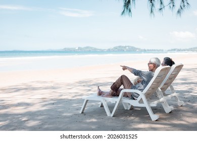 Retired Couple Resting On A Adirondack Chair By The Beach In The Sunlight And Clean Sandy Beach. Retirement Planning Ideas And Happy Life.