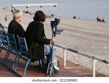 A Retired Couple Sits On The Beach In Nice. She Uses On Crutches, 19.02.2020