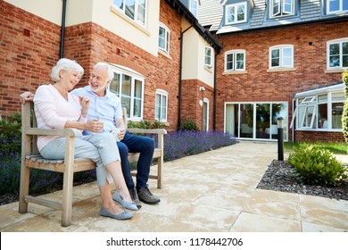 Retired Couple Sitting On Bench With Hot Drink In Assisted Living Facility