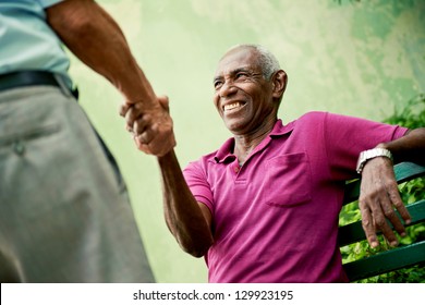 Retired Elderly People And Free Time, Happy Senior African American And Caucasian Male Friends Greeting And Sitting On Bench In Park
