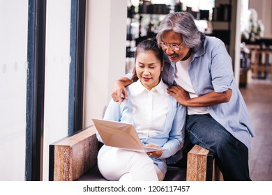 Retired And Elderly South East Asian Senior Male And Female Couple Using Computer Laptop Together On Sofa Indoors