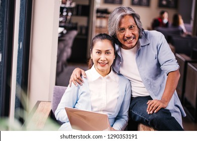 Retired And Elderly South East Asian Senior Male And Female Couple Using Computer Laptop Together On Sofa Indoors