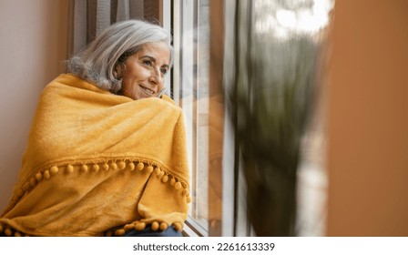 Retired elderly woman, in her cozy home with the heater on while looking out the window on a winter day - Powered by Shutterstock