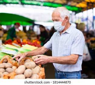 pensionierter europäischer Mann mit medizinischer Maske, der sich vor dem Kauf von Kartoffeln auf dem Markt schützt