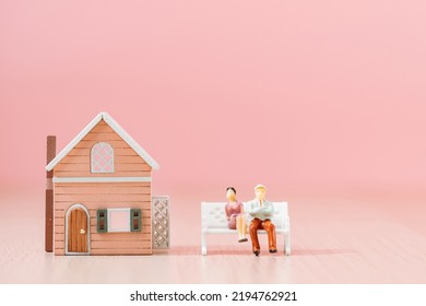 Retired Husband And Wife Couple Model Sitting On A Bench And Home Sweet Home On The Pink Background In The Office, Saving Money For Retirement And Planning In The Future Concept.