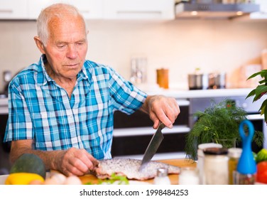 Retired Man Preparing Fish At Home In The Kitchen