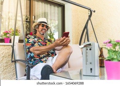Retired Man Using Phone While Listening Music at Home . Pensioner Man Having Fun and Listening Music From an Old Radio Cassette. Old Man Enjoying Summer Time. Lifestyle Concept.