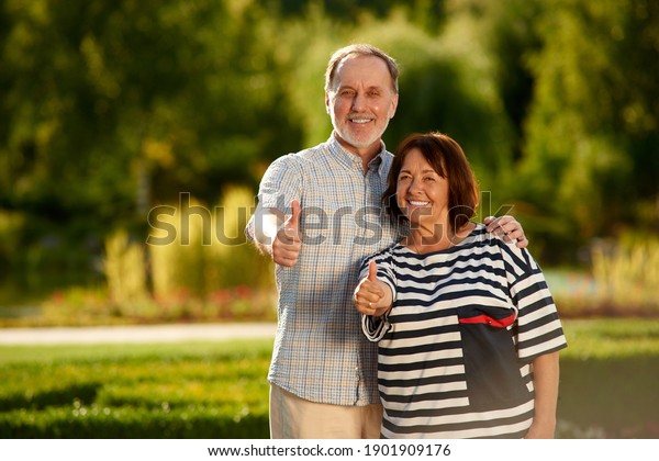 Retired married couple shows thumbs up. Old man and\
woman in the summer\
park.