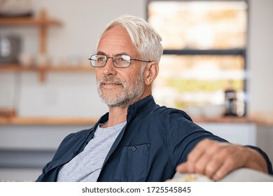 Retired Mature Man Sitting On Couch Wearing Spectacles And Thinking. Smiling Old Man Planning The Retirement. Thoughtful Senior Business Man Relaxing At Home While Looking Away With Copy Space. 