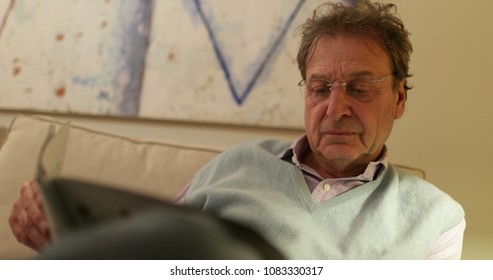 Retired Older Man Reading Magazine On Living-room Sofa. Candid Real Life Moment Retired Man Casually Reading News On Sofa