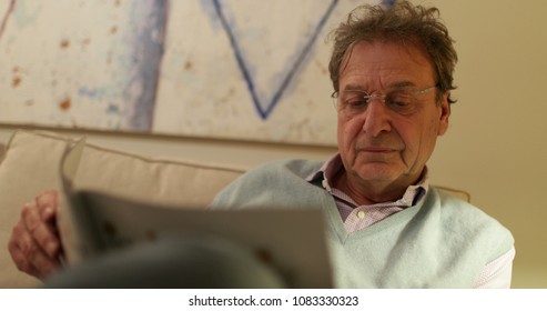 Retired Older Man Reading Magazine On Living-room Sofa. Candid Real Life Moment Retired Man Casually Reading News On Sofa