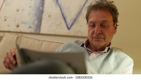 Retired Older Man Reading Magazine On Living-room Sofa. Candid Real Life Moment Retired Man Casually Reading News On Sofa