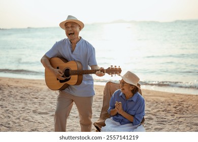 retired, retirement, couple, senior, elderly, beach, recreation, insurance, planning, vacation. A man and woman are playing guitar on a beach. The man is smiling and the woman is laughing. - Powered by Shutterstock