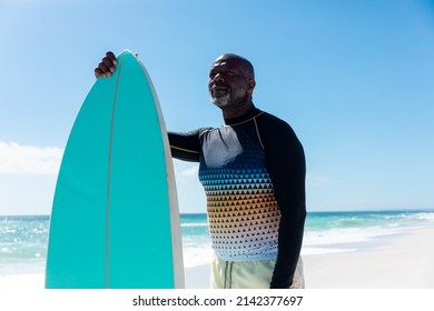 Retired senior african american man holding surfboard standing at beach against blue sky. unaltered, active lifestyle, aquatic sport and holiday concept. - Powered by Shutterstock