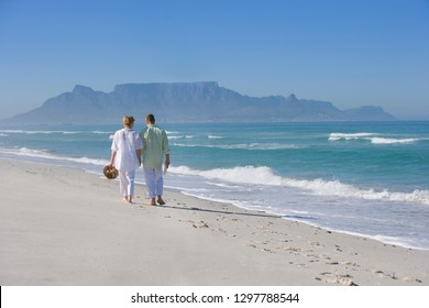 Retired Senior Couple Walking Away From Camera On Beach Vacation