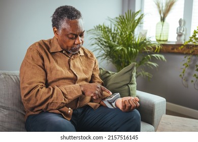 Retired Senior Man Examining Blood Pressure In Living Room Of Apartment. Male Is Holding Diagnostic Medical Tool While Sitting At Home. He Is In Residential Building.