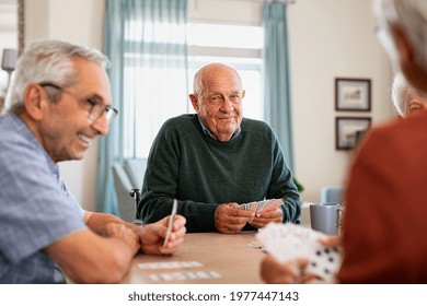 Retired Senior Man In Wheelchair Playing Cards With Friends At Nursing Home. Smiling Group Of Old People Playing Cards At Care Centre. Happy Seniors Playing At Lunch Table And Having Fun Together.