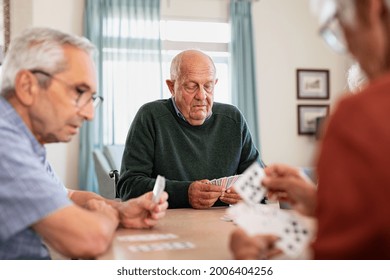 Retired senior man in wheelchair playing cards with his friends at nursing home. Group of old friends playing cards at care centre. Focused senior people playing cards game during afternoon. - Powered by Shutterstock